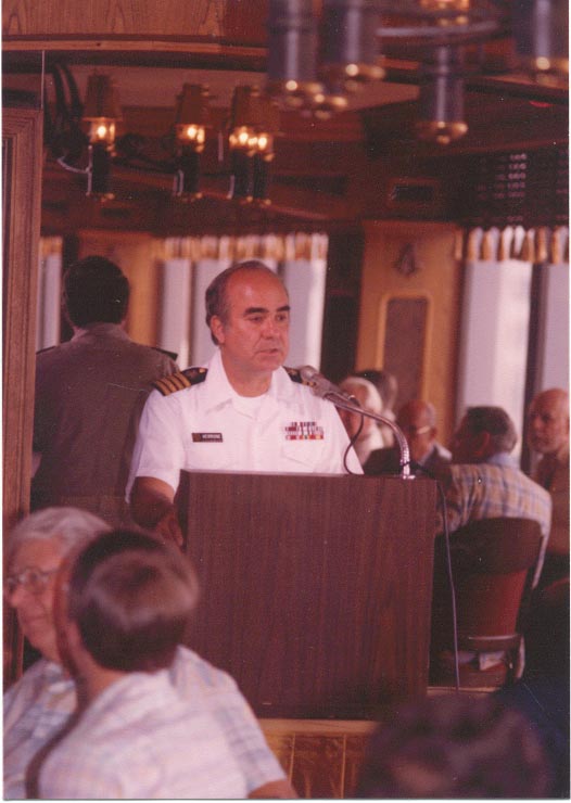 CAPT Verrone in summer white uniform standing behind a podium making a presentation